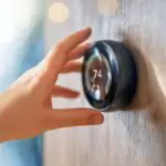 hand adjusting a thermostat set at 74 degrees